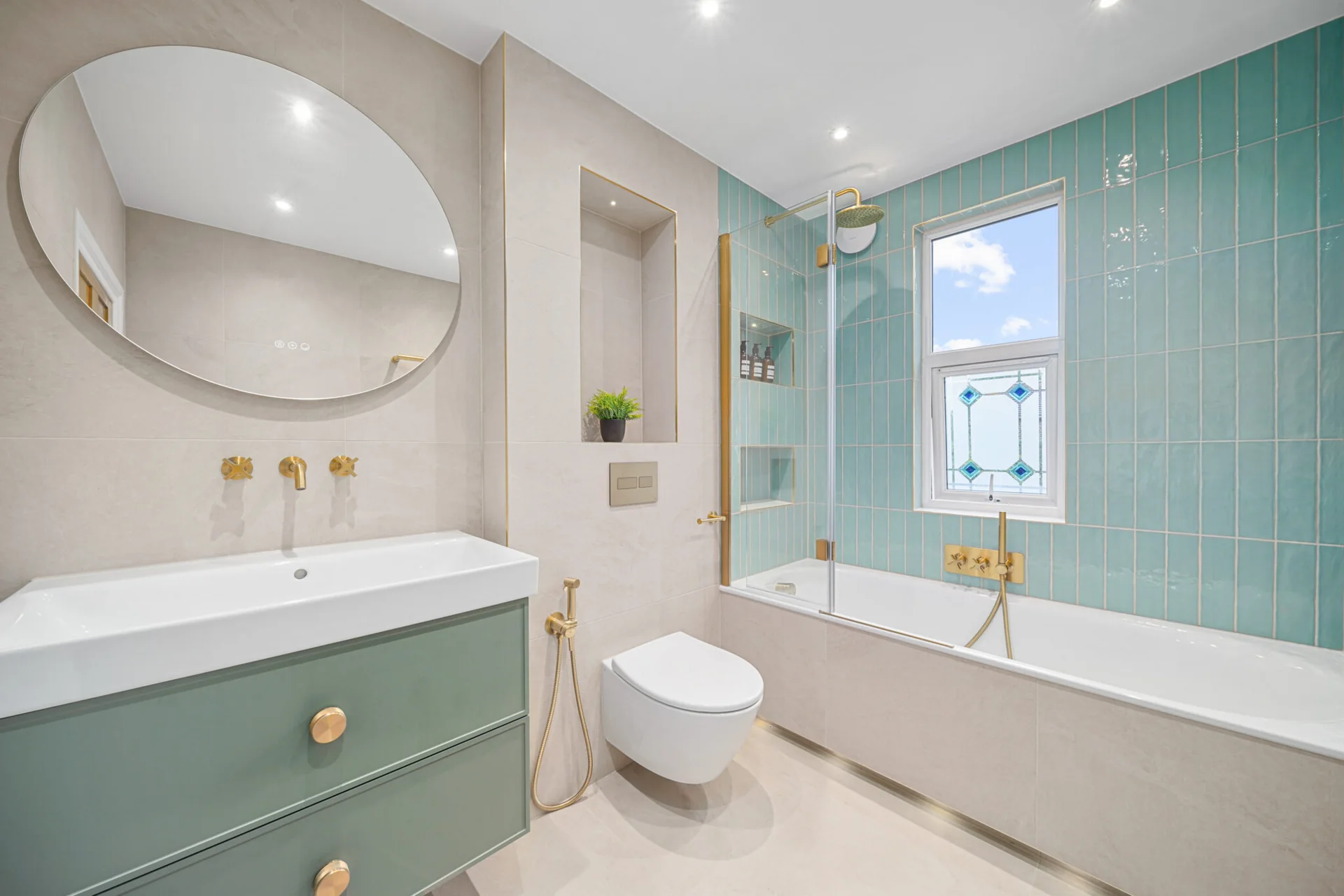 Completed family bathroom with mint-green furniture and tiles, a bath and an oval mirror.